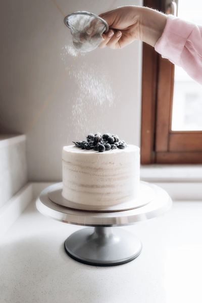 Baker dusting powdered sugar over a blueberry cake